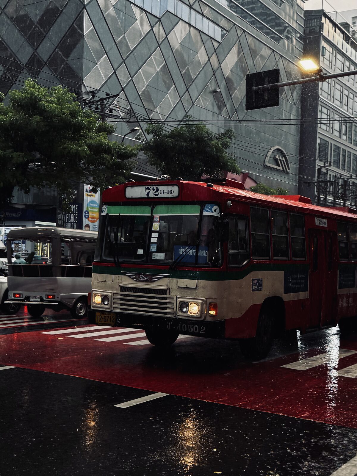 A red number 72 bus crossing a wet intersection in Bangkok