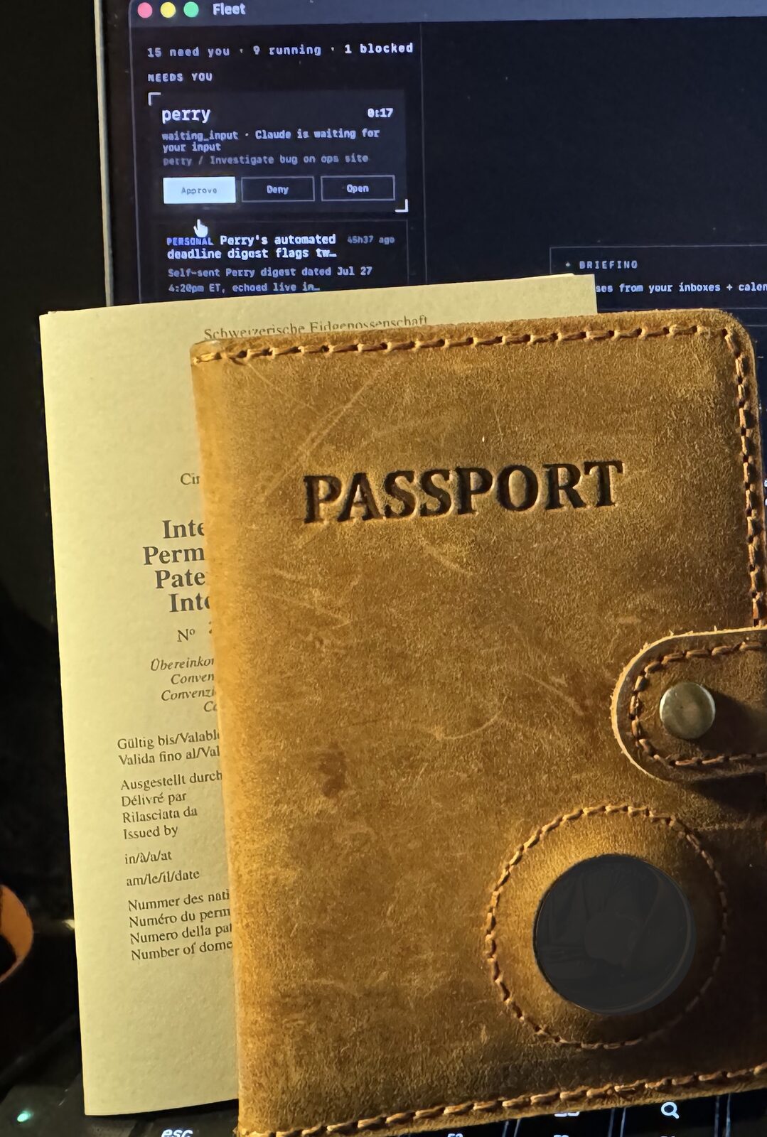 A leather passport wallet and the Swiss international driving permit, propped against a laptop showing the Fleet dashboard waiting for input